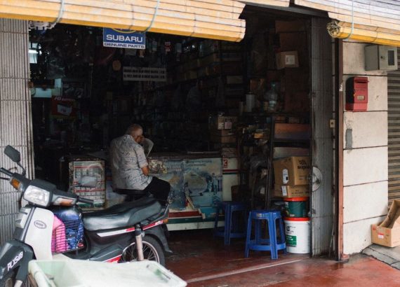 Ejer af en reservedelsbutik sidder ved disken bag en scooter.