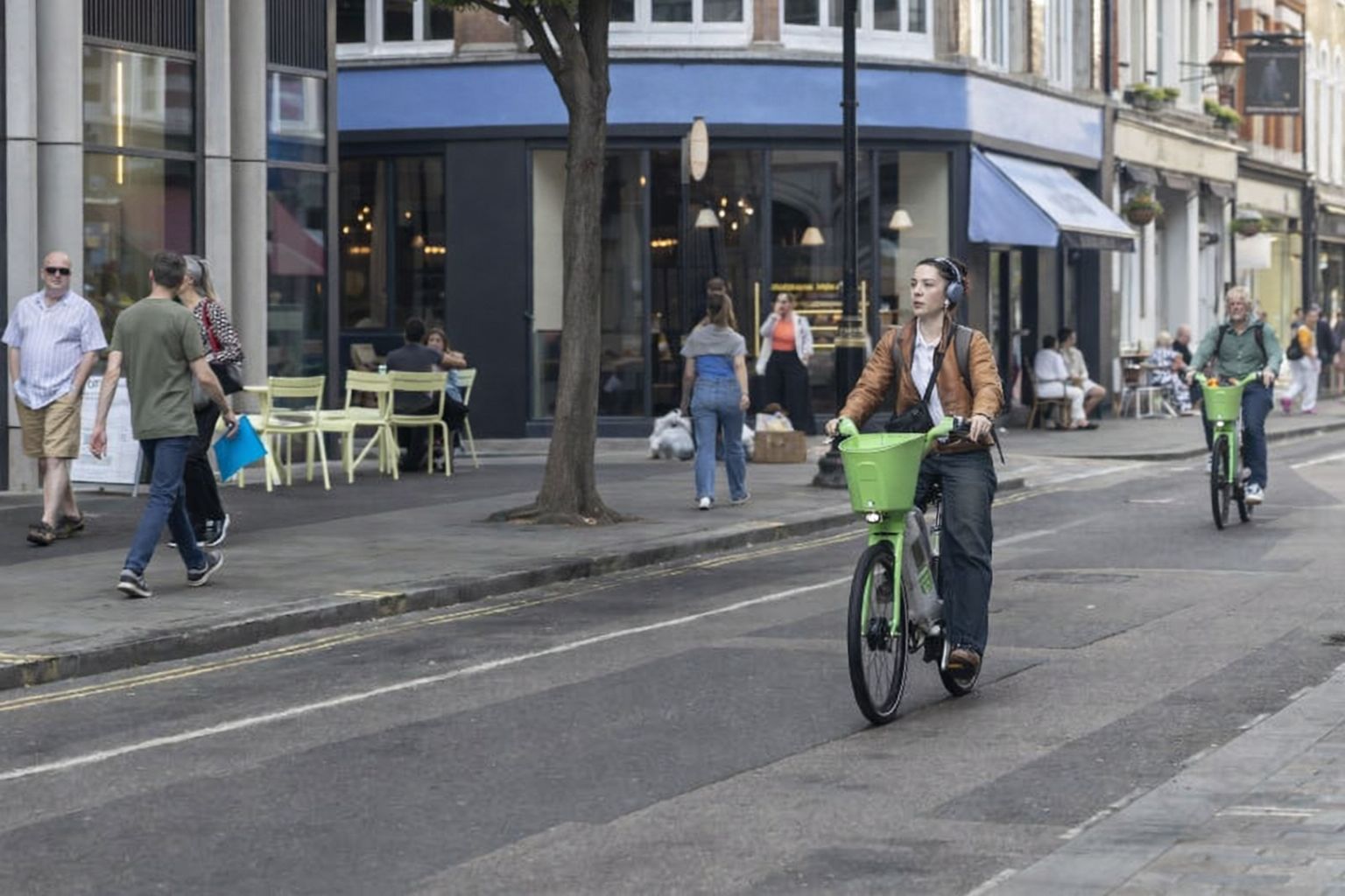 Folk cykler og går langs en bygade med caféer og butikker.