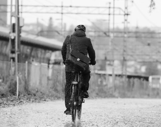 Cyklist med hjelm cykler gennem regnen med taske på ryggen
